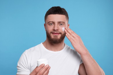 Photo of Handsome man applying cream onto his face on light blue background