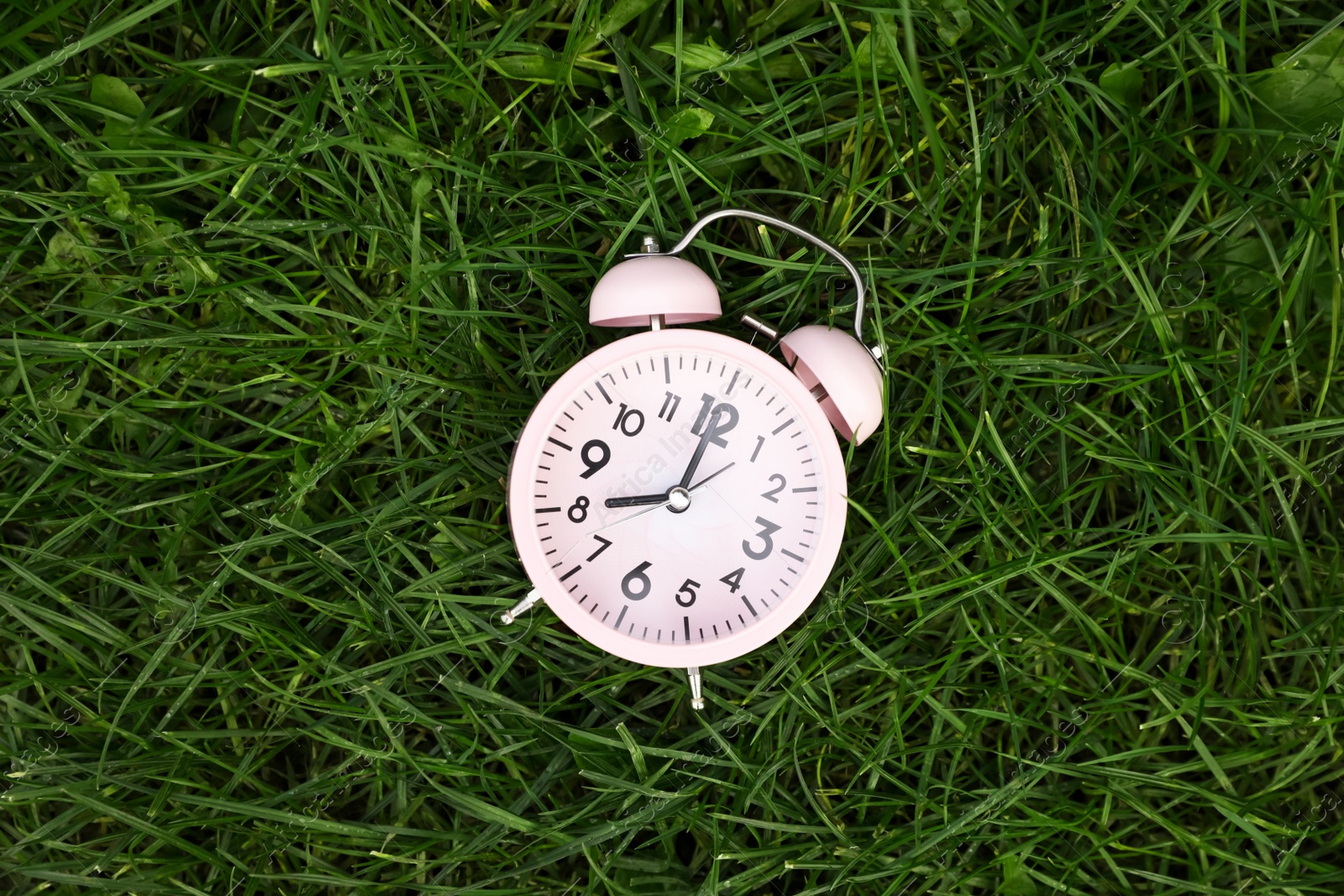 Photo of Pink small alarm clock on green grass outdoors, top view