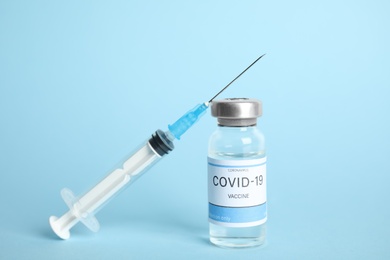 Photo of Vial with coronavirus vaccine and syringe on light blue background
