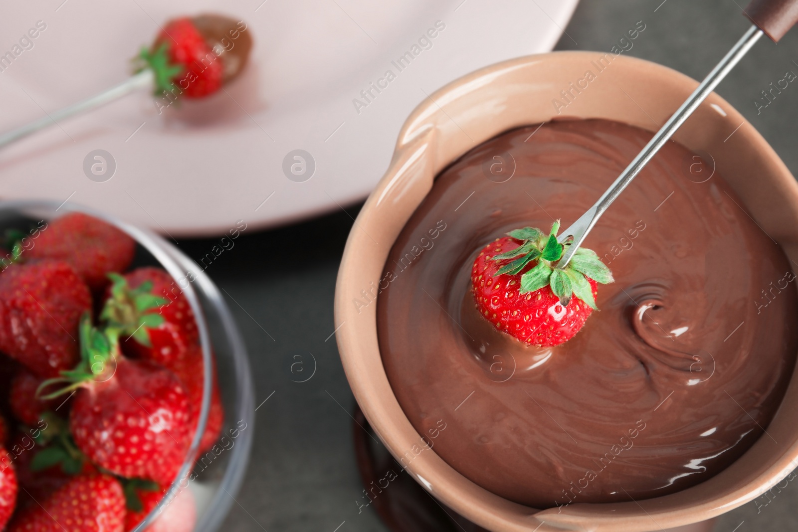 Photo of Ripe strawberry dipping into chocolate fondue, closeup