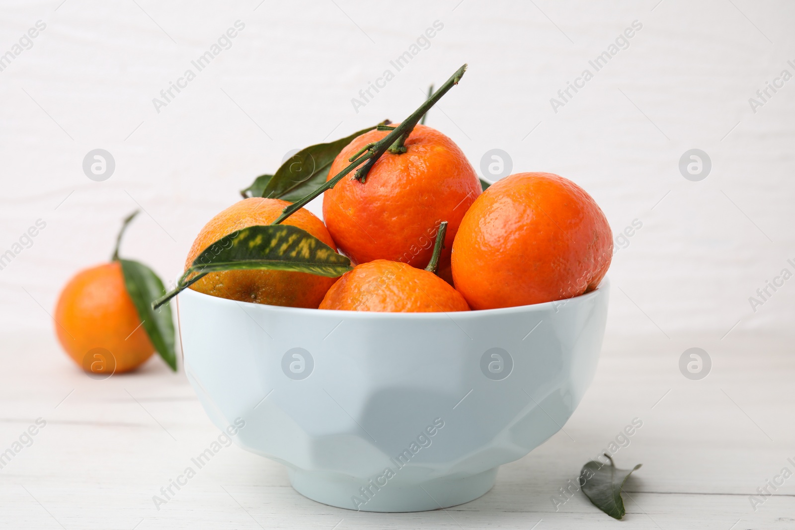 Photo of Bowl with fresh ripe tangerines and leaves on white table