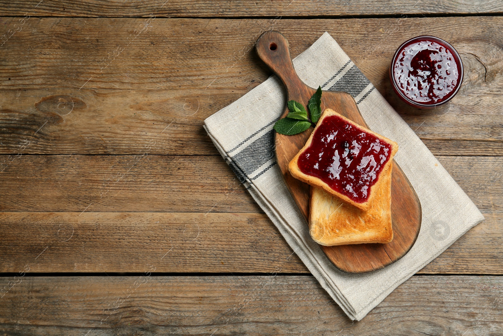 Photo of Delicious toasts served with jam and mint on wooden table, flat lay. Space for text