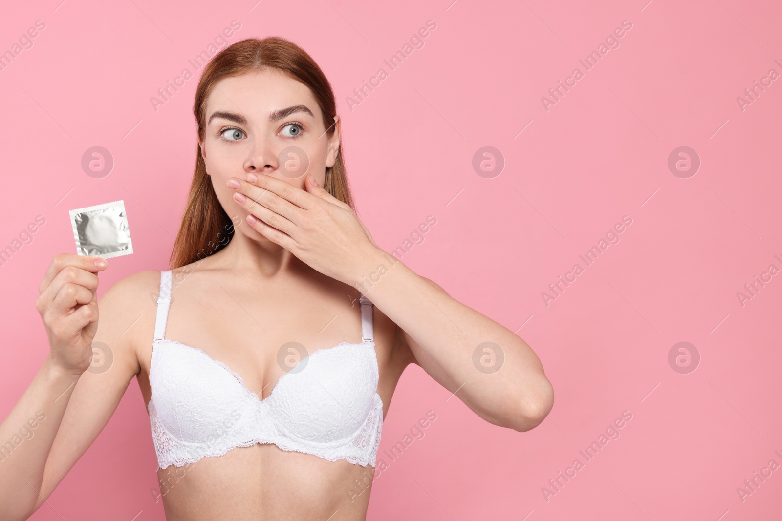 Photo of Woman in bra holding condom on pink background, space for text. Safe sex