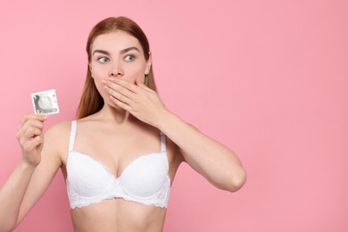 Photo of Woman in bra holding condom on pink background, space for text. Safe sex