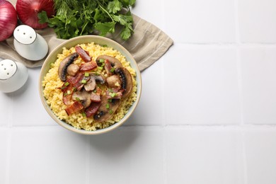 Tasty millet porridge with mushrooms, bacon and green onion in bowl on white tiled table, flat lay. Space for text