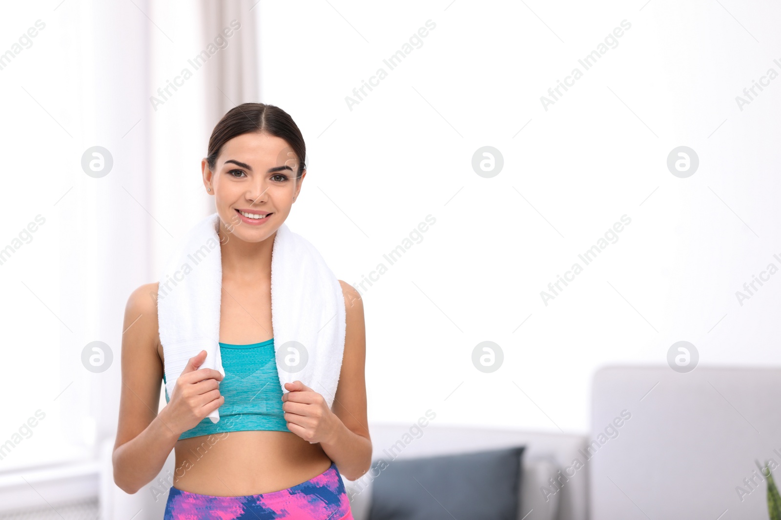 Photo of Beautiful young woman in sportswear with towel indoors. Space for text