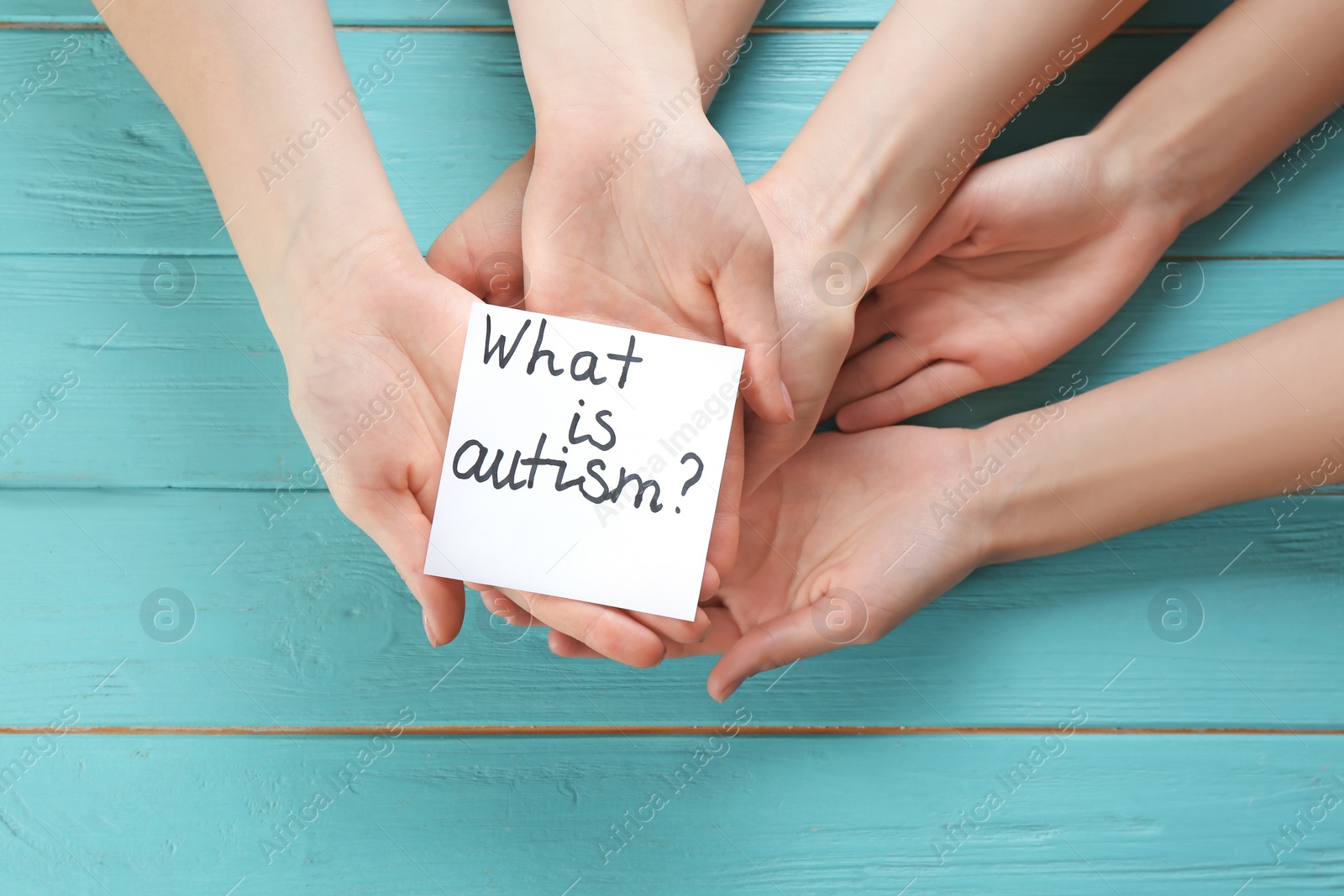 Photo of Group of people holding note with phrase "What is autism?" on wooden background