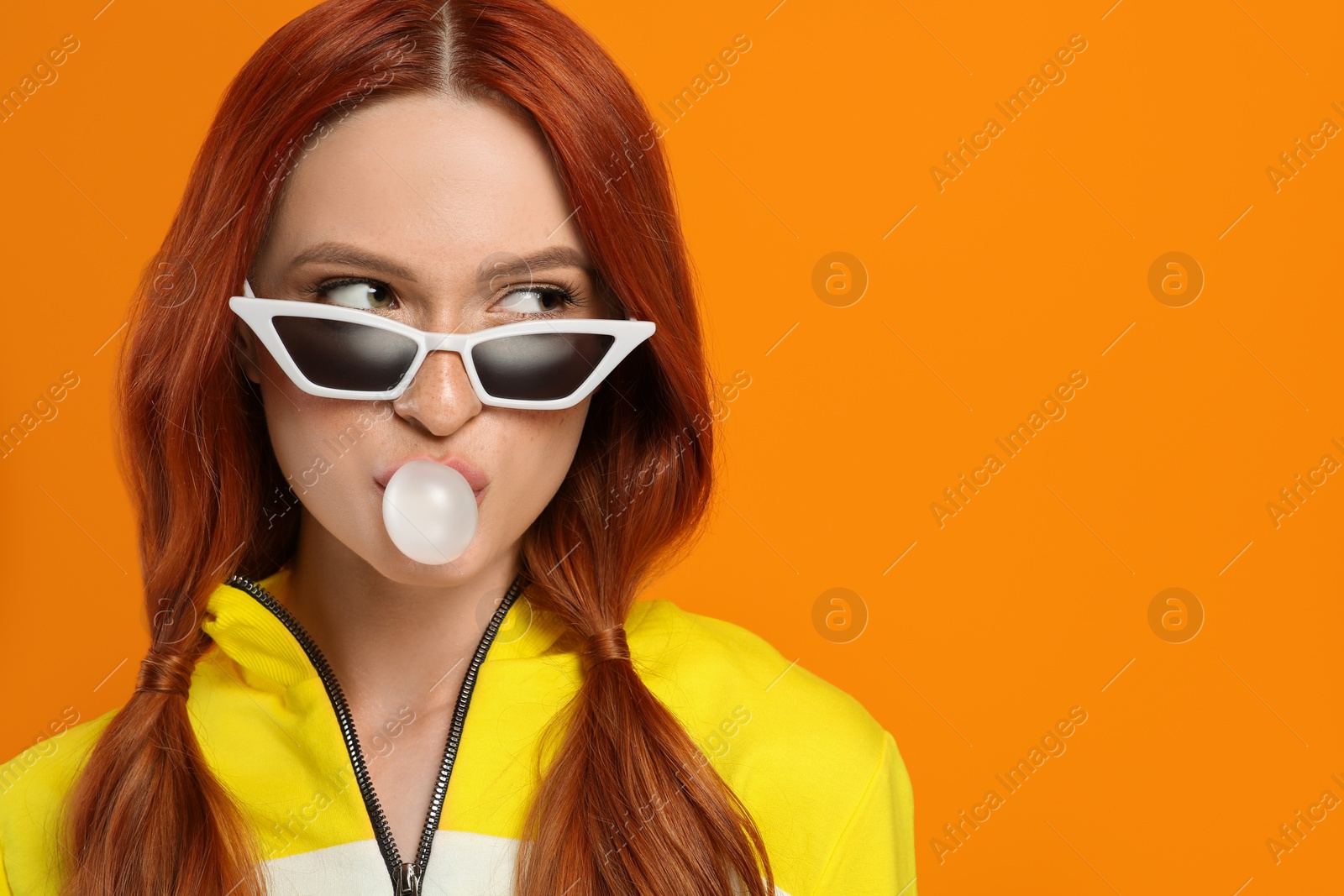 Photo of Beautiful woman in sunglasses blowing bubble gum on orange background. Space for text