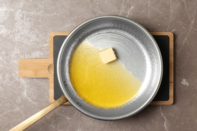 Frying pan with melting butter on grey background, top view
