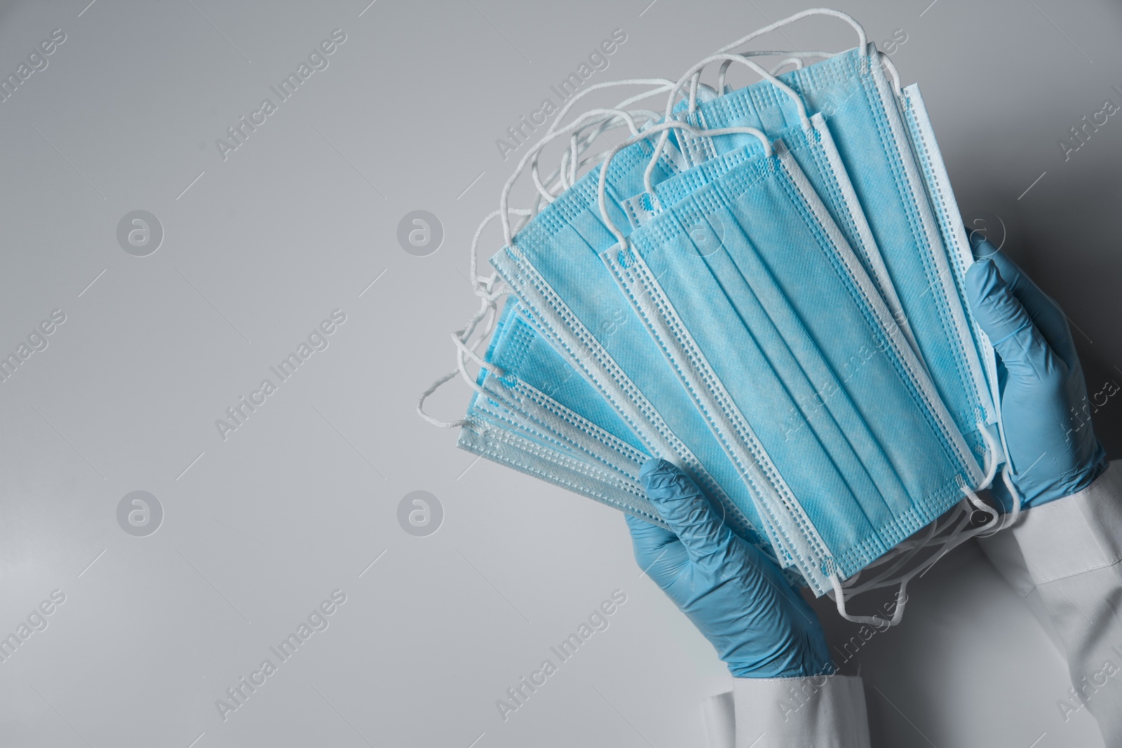 Photo of Doctor in latex gloves holding disposable face masks on light background, closeup with space for text. Protective measures during coronavirus quarantine