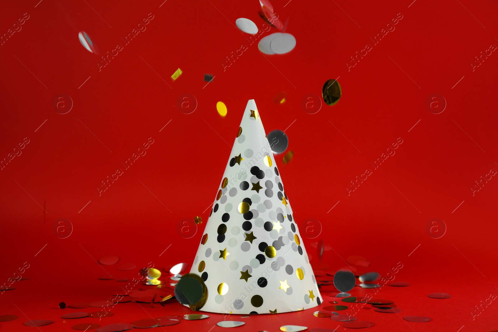 Photo of White party hat and confetti on red background