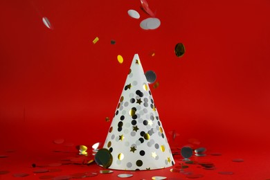 Photo of White party hat and confetti on red background