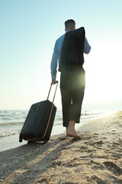 Photo of Businessman with suitcase walking on beach, low angle view. Business trip