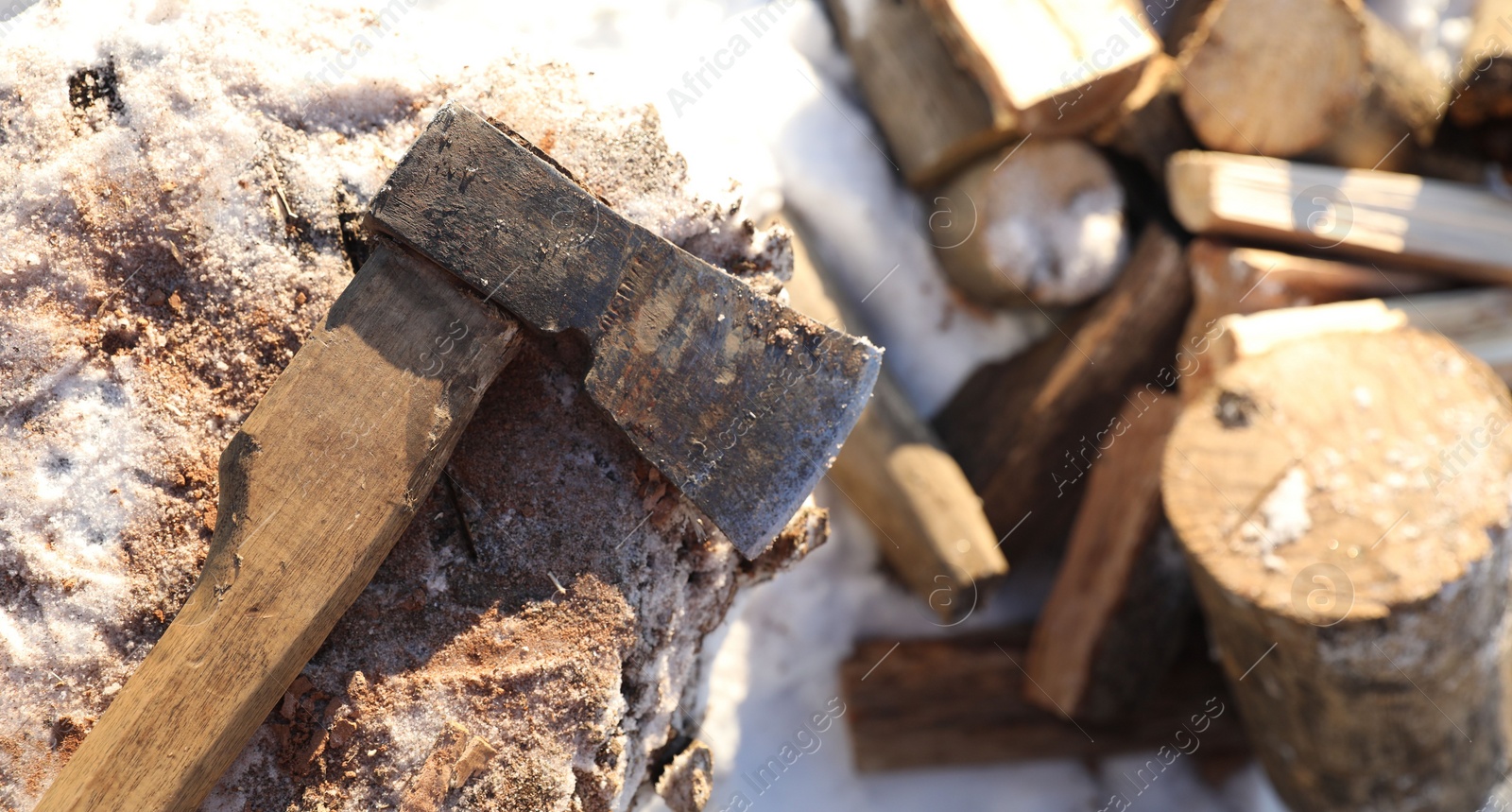 Photo of Metal axe on wooden log and pile of wood outdoors on sunny winter day, top view. Space for text
