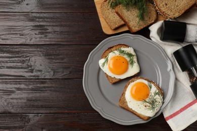 Photo of Plate with tasty fried eggs, slices of bread and dill on dark wooden table, flat lay. Space for text