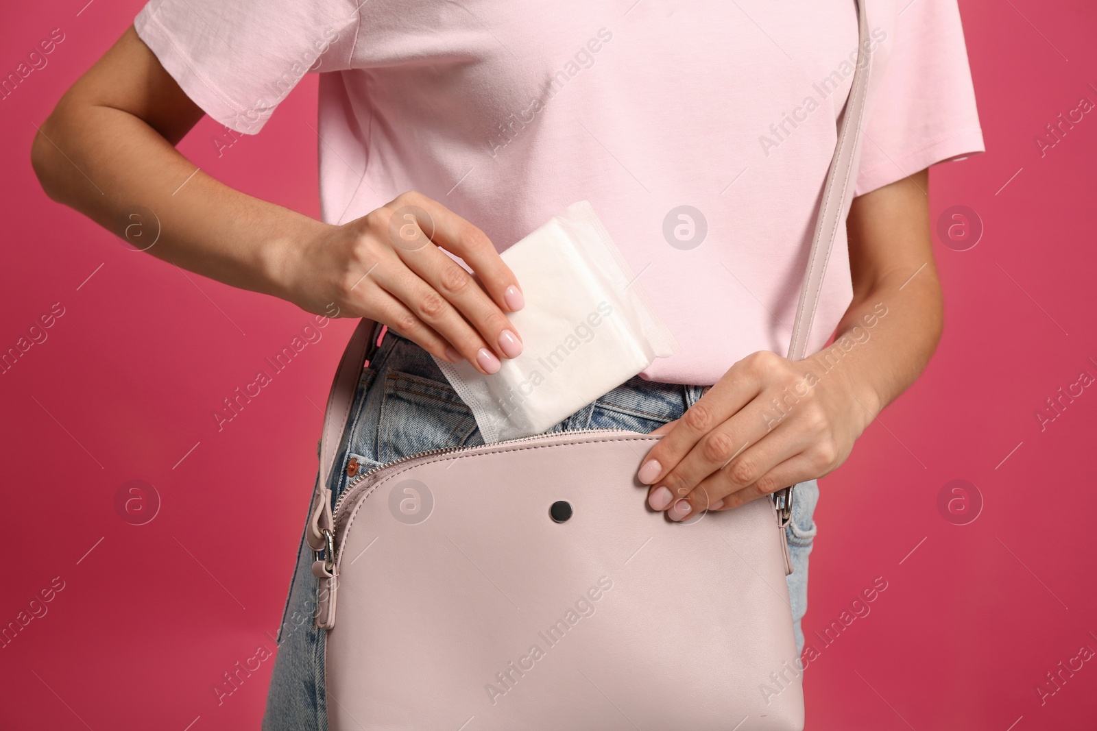 Photo of Young woman putting menstrual pad into purse on bright pink background, closeup