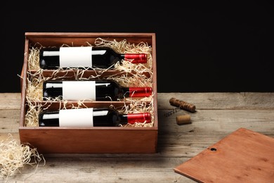 Box with wine bottles on wooden table against black background. Space for text