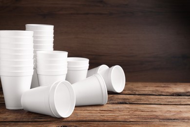 Photo of Many white styrofoam cups on wooden table, space for text