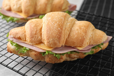 Photo of Tasty croissant sandwiches with ham on rack, closeup