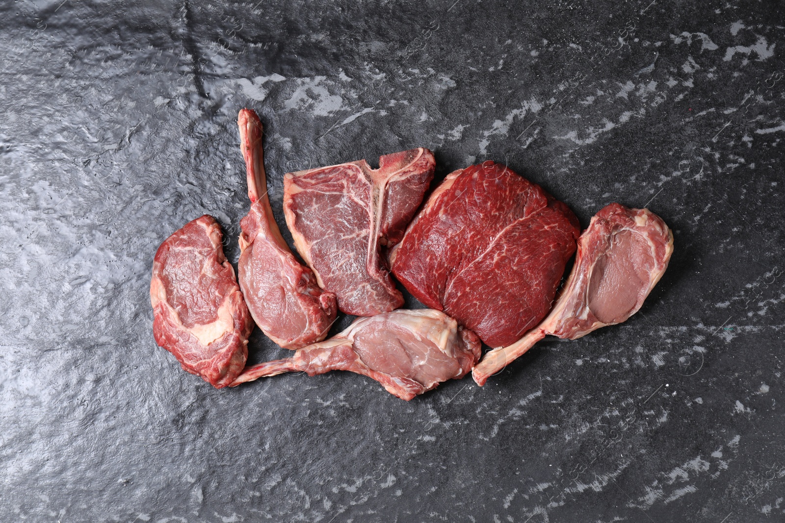 Photo of Fresh raw beef cuts on grey textured table, flat lay