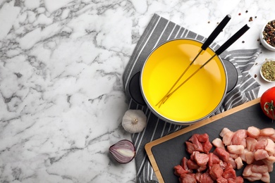 Flat lay composition with fondue pot, raw meat and space for text on marble background