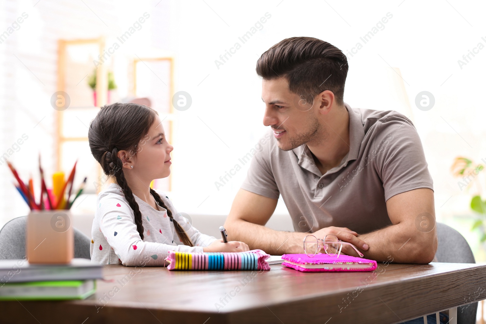 Photo of Man helping his daughter with homework at table indoors