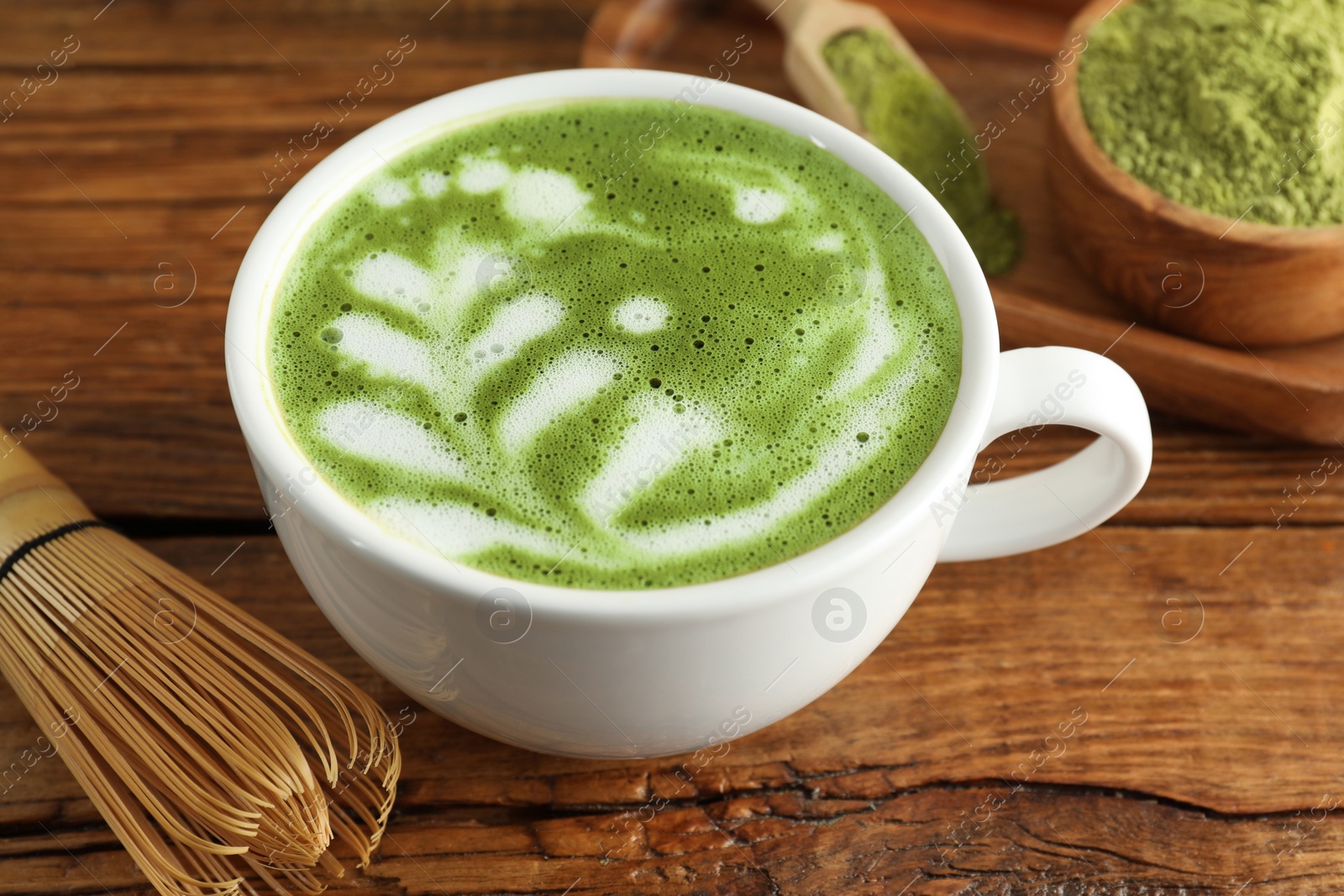 Photo of Cup of fresh matcha latte and bamboo whisk on wooden table, closeup