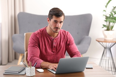 Photo of Handsome young man working with laptop at table in office