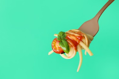 Tasty pasta with tomato sauce and basil on fork against green background, closeup. Space for text