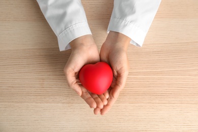 Photo of Doctor holding red heart on wooden table, top view. Cardiology concept
