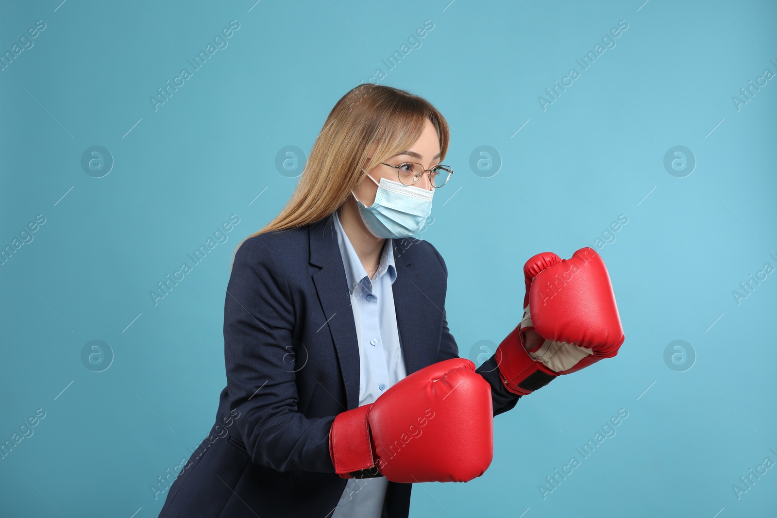 Photo of Businesswoman with protective mask and boxing gloves on light blue background. Strong immunity concept