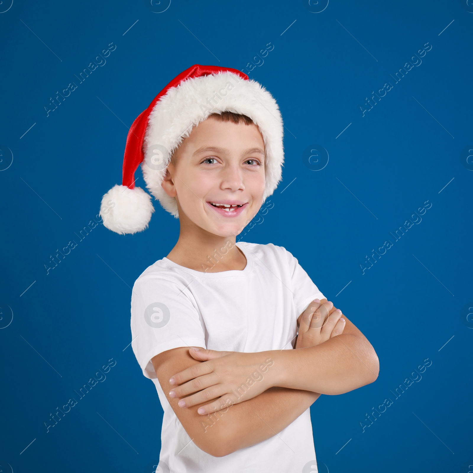 Image of Happy little child in Santa hat on blue background. Christmas celebration