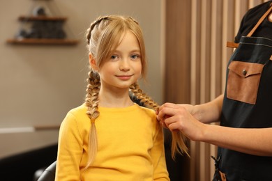 Professional hairdresser braiding girl's hair in beauty salon