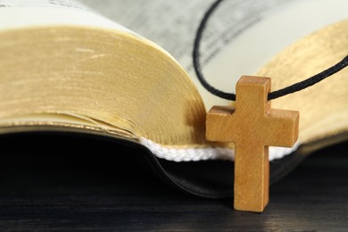 Christian cross and Bible on black wooden table, closeup