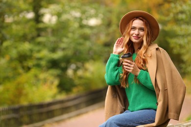 Photo of Portrait of beautiful woman with paper cup in autumn park. Space for text