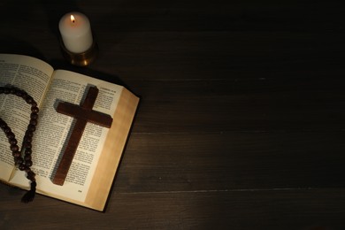 Photo of Church candle, Bible, rosary beads and cross on wooden table, top view. Space for text