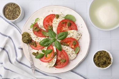 Photo of Plate of delicious Caprese salad with pesto sauce on white tiled table, flat lay