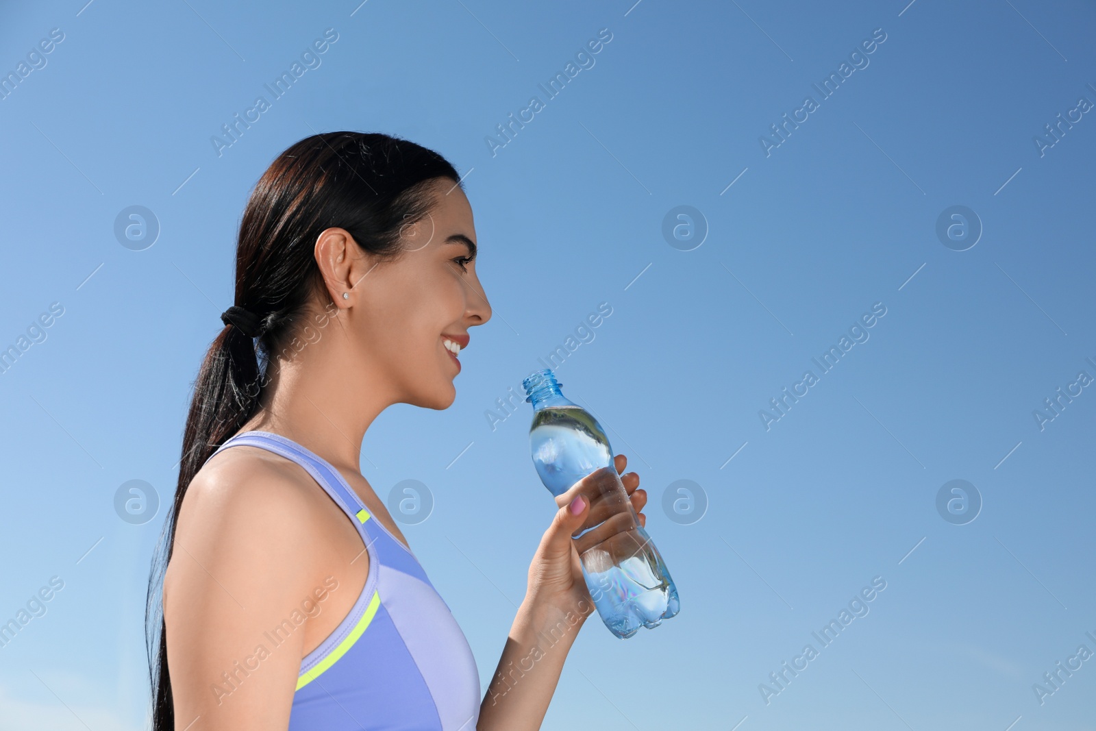 Photo of Beautiful young sportswoman with bottle of water outdoors. Refreshing drink