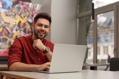 Photo of Young male business owner working with laptop in his cafe