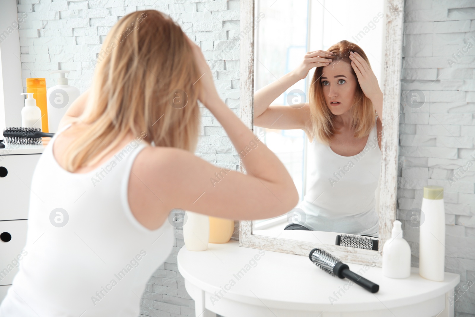 Photo of Young woman with hair loss problem in front of mirror at home