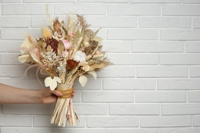 Photo of Woman holding beautiful dried flower bouquet near white brick wall, closeup. Space for text