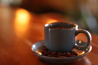 Photo of Cup of hot aromatic coffee and roasted beans on wooden table in cafe. Space for text