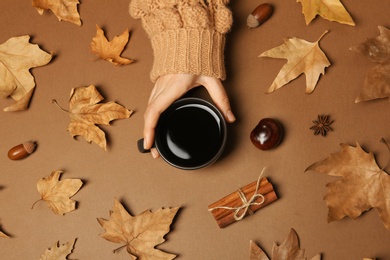 Photo of Woman in autumn sweater holding cup of hot cozy drink on color background, top view