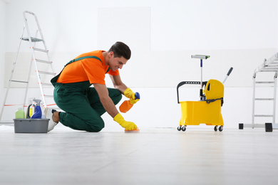 Photo of Professional janitor cleaning floor with brush and detergent after renovation