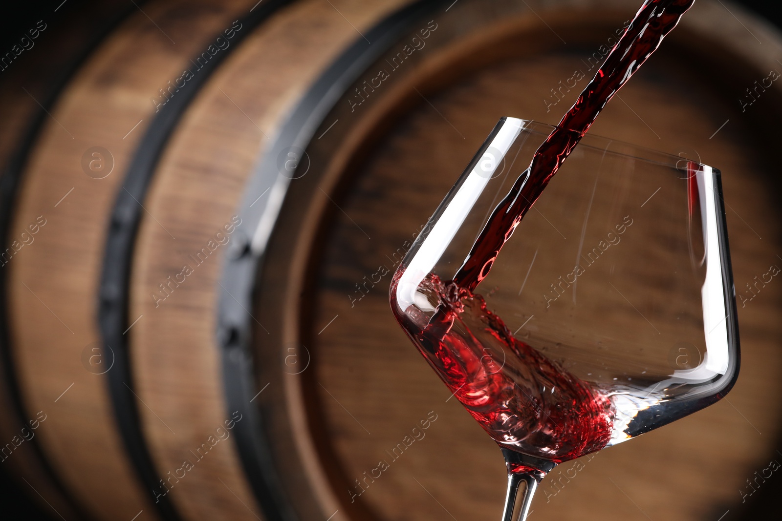 Photo of Pouring red wine into glass near wooden barrel, closeup. Space for text