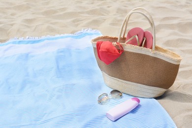 Photo of Light blue striped towel with bag, flip flops, sunglasses and sunblock on sandy beach