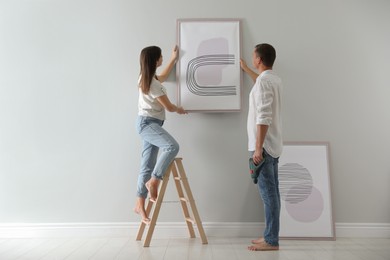 Photo of Couple hanging picture on wall together in room. Interior design