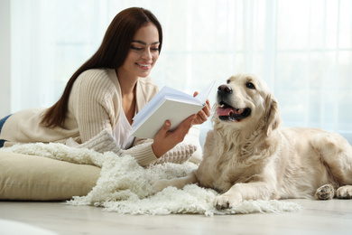 Young woman with book and her Golden Retriever at home. Adorable pet