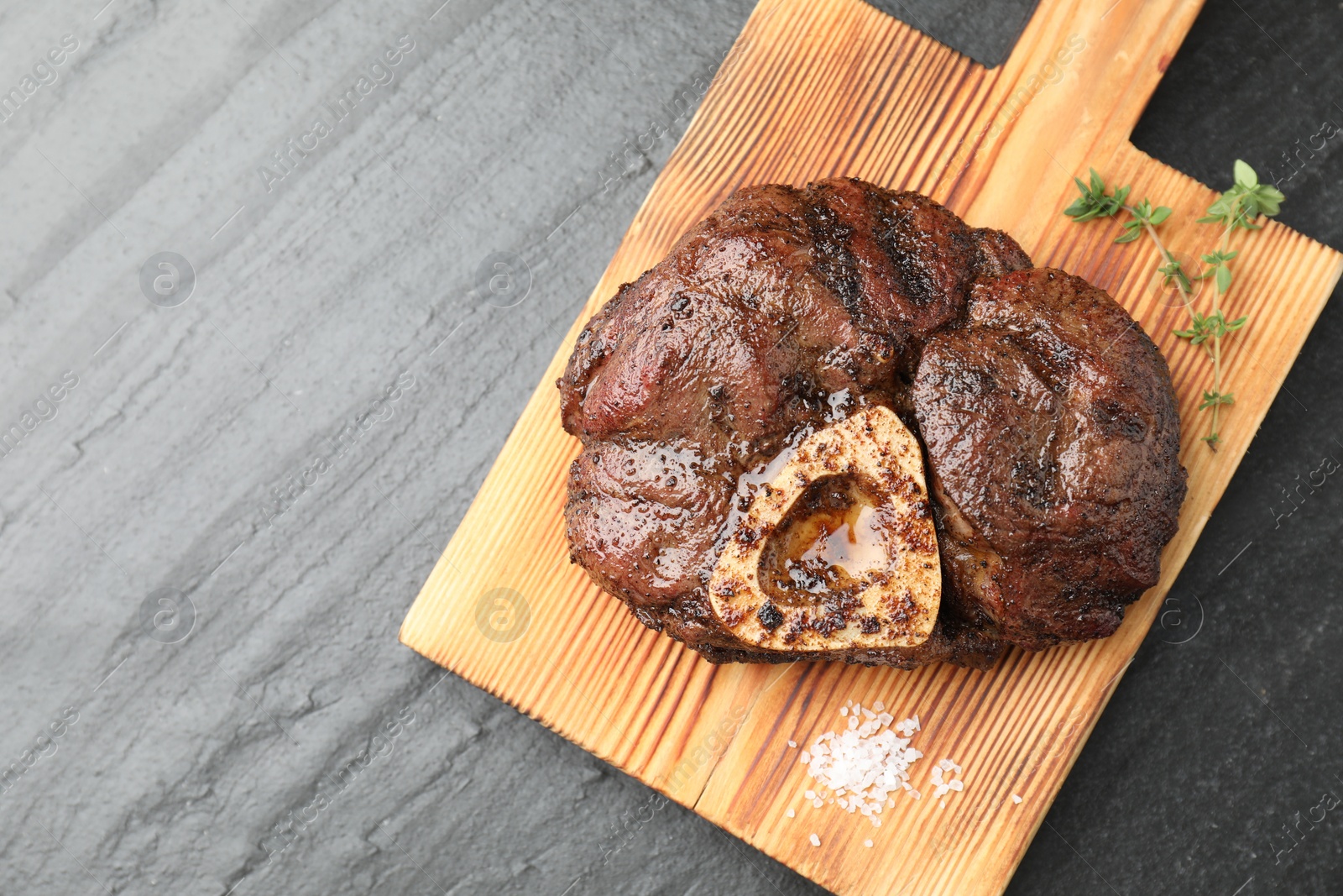 Photo of Piece of delicious grilled beef meat, thyme and salt on black table, top view. Space for text