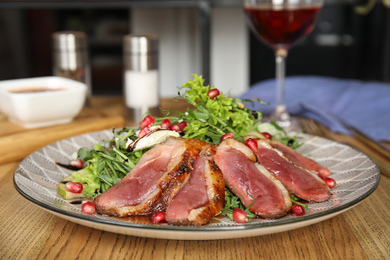 Photo of Delicious salad with roasted duck breast served on wooden table indoors